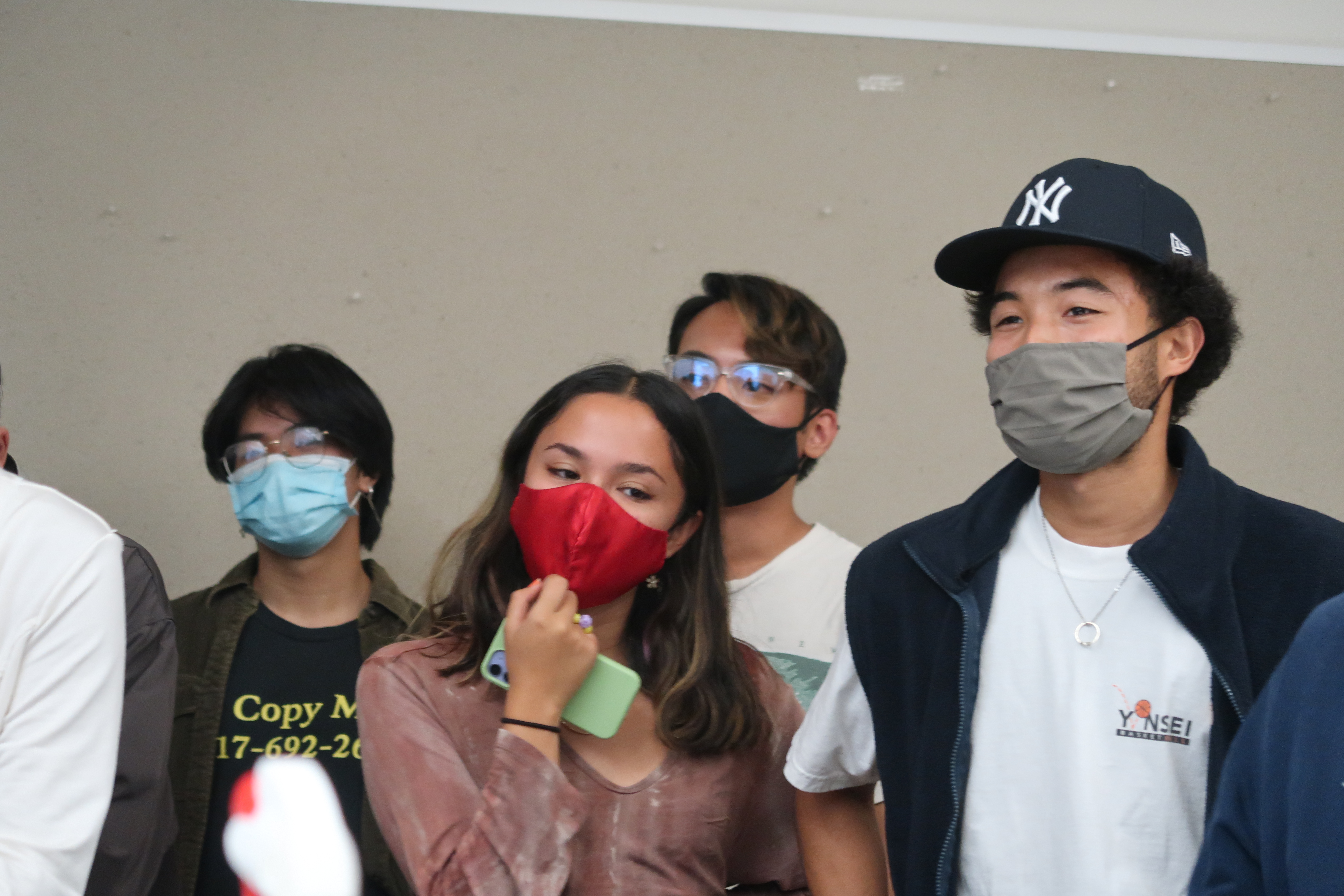 Students with varying face mask colors of red, blue, black, and gray smiling and looking at camera.